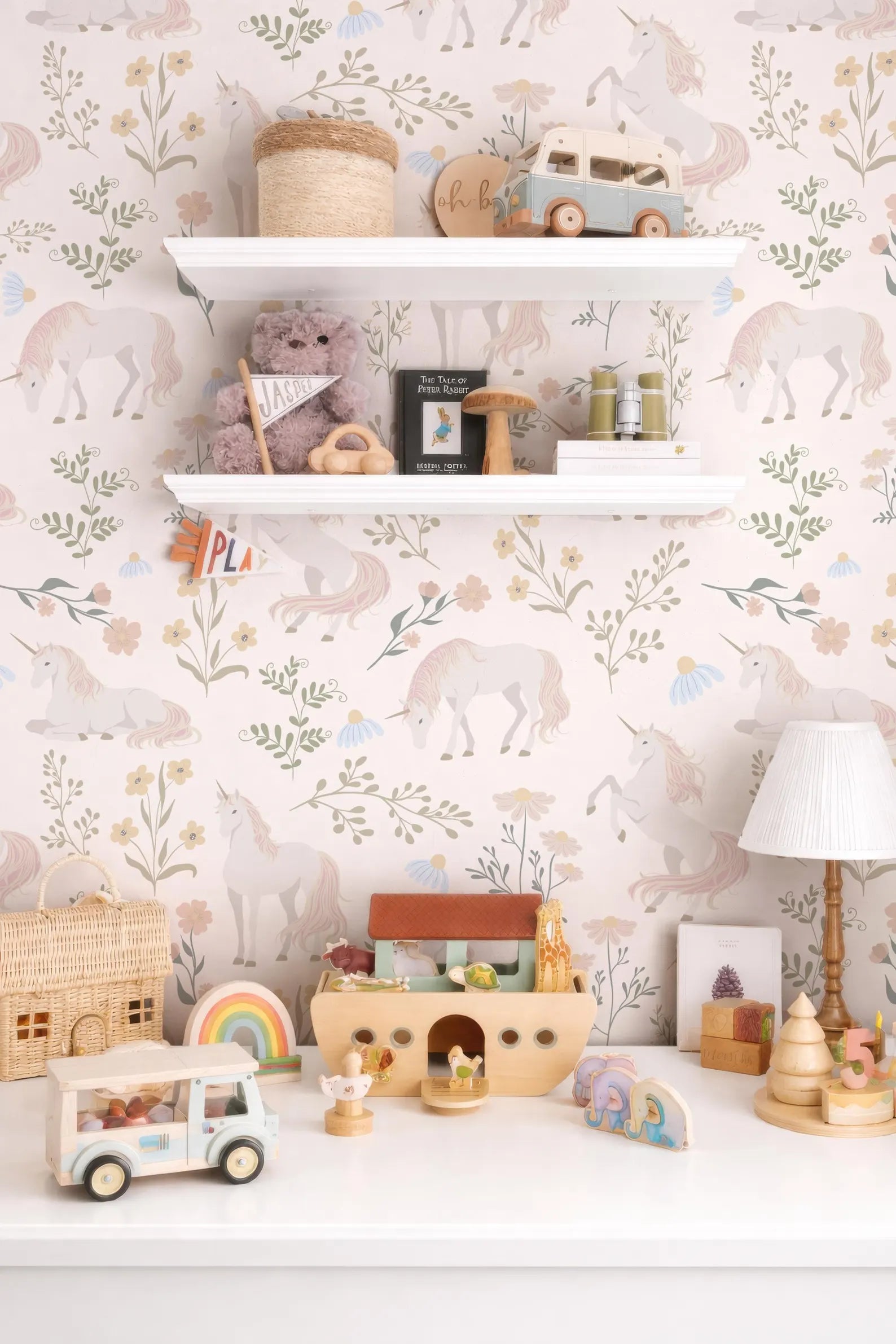 a child's bedroom with a white shelf displaying various toys and decorative items, including a toy car, a toy castle, and a toy truck. The wall behind the shelf has a floral wallpaper pattern, and there is a rainbow-colored toy car on the shelf.