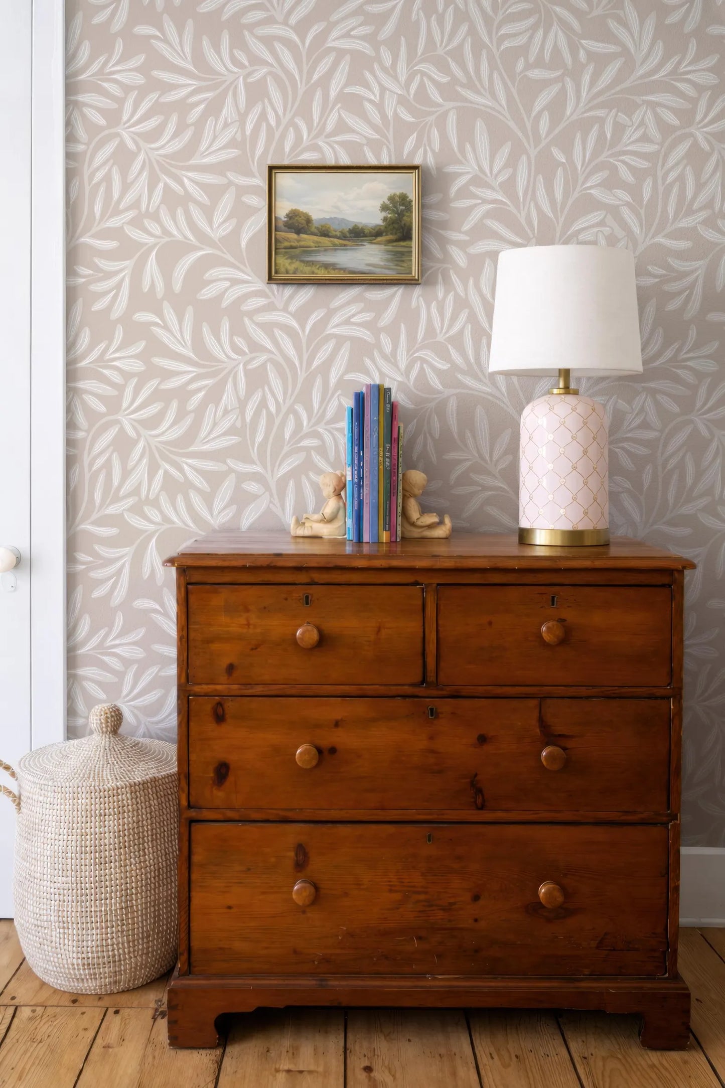 a wooden dresser with a lamp and a basket on top, set against a wall with a framed landscape painting.