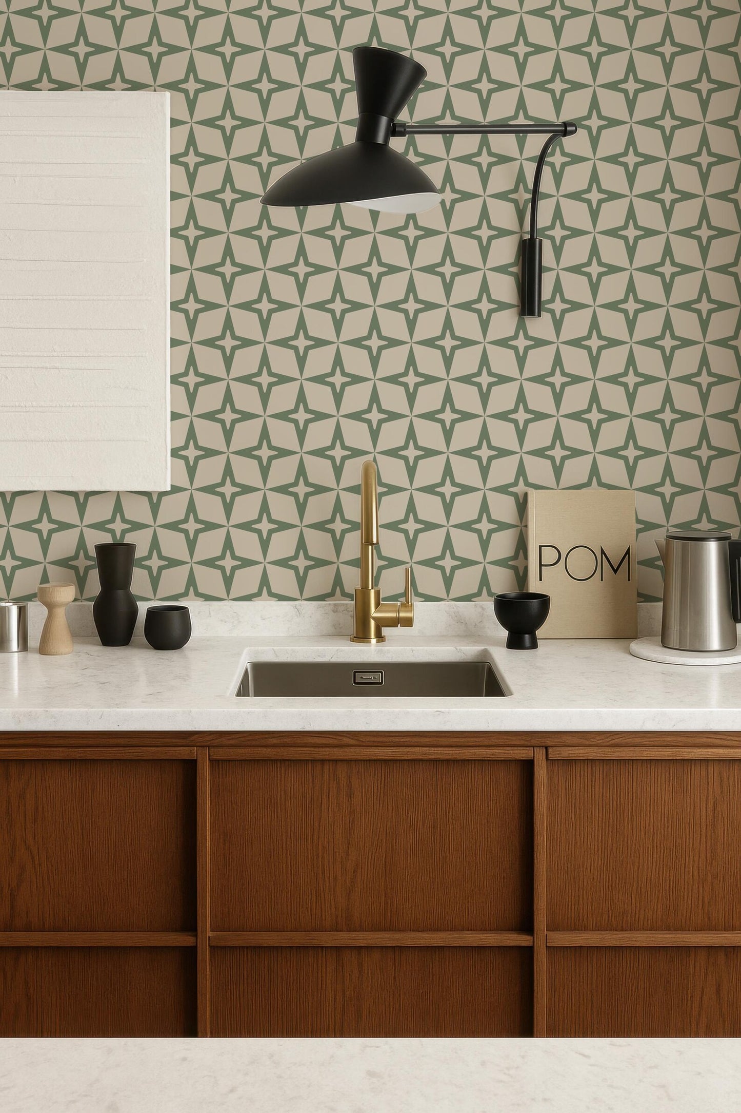 a modern kitchen with a white countertop, wooden cabinets, and a gold faucet above the sink. The walls are adorned with a geometric pattern wallpaper, and a black pendant light hangs above the sink. The kitchen also includes various decorative elements such as a bowl, a vase, and a book.