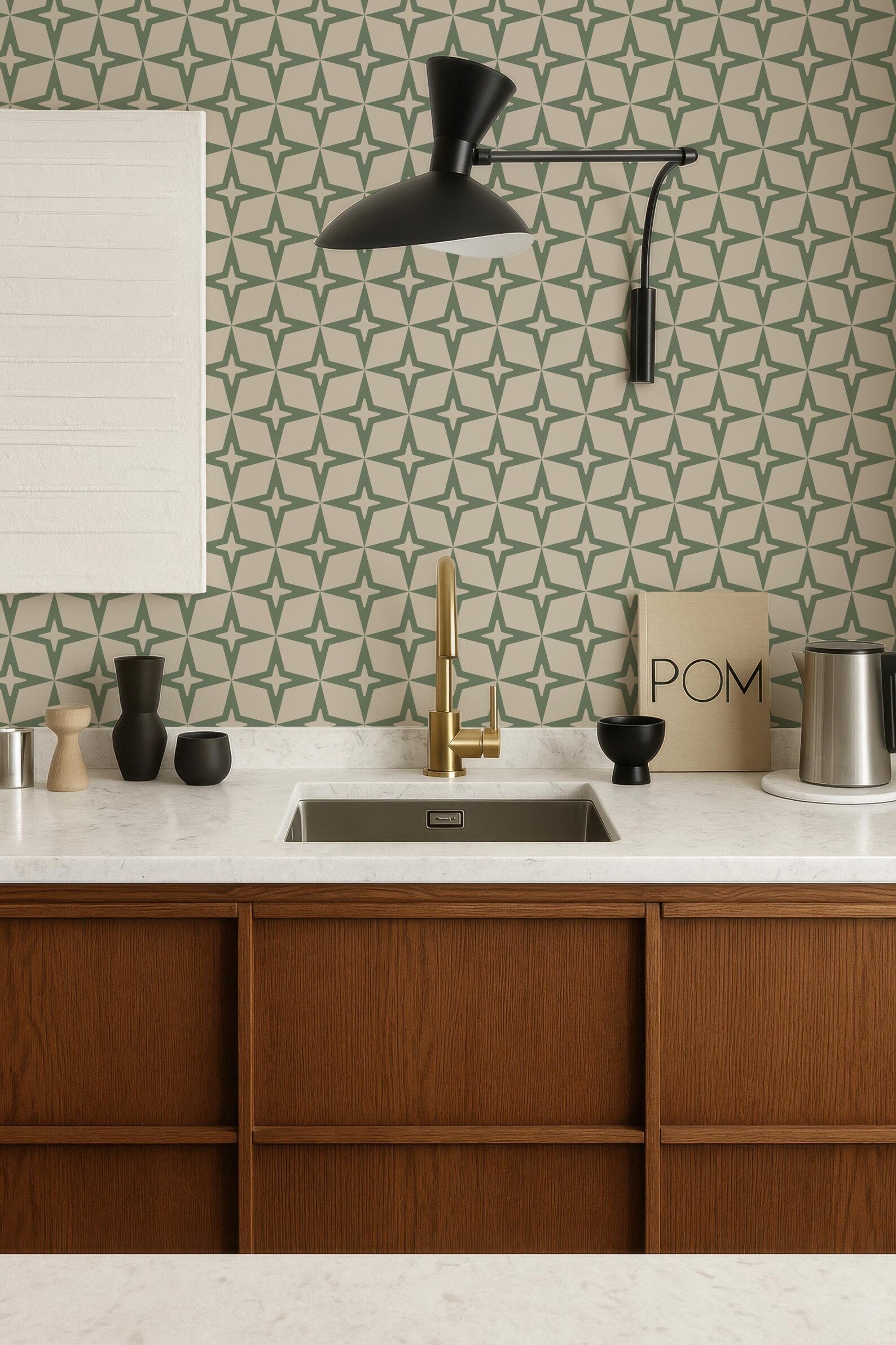a modern kitchen with a white countertop, wooden cabinets, and a gold faucet above the sink. The walls are adorned with a geometric pattern wallpaper, and a black pendant light hangs above the sink. The kitchen also includes various decorative elements such as a bowl, a vase, and a book.