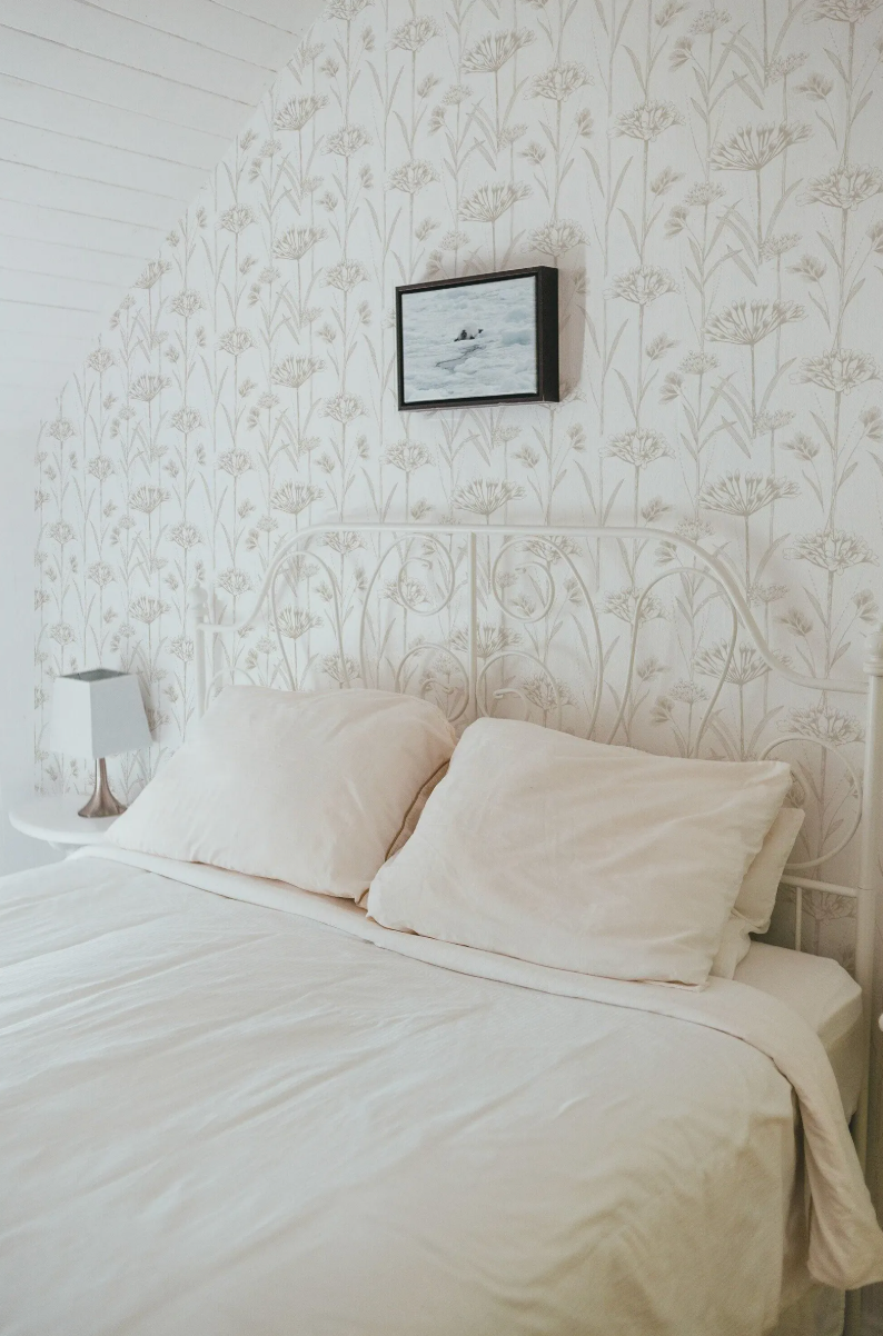 a cozy bedroom with a white metal headboard and two white pillows on a bed. Above the bed, there is a framed picture hanging on the wall.