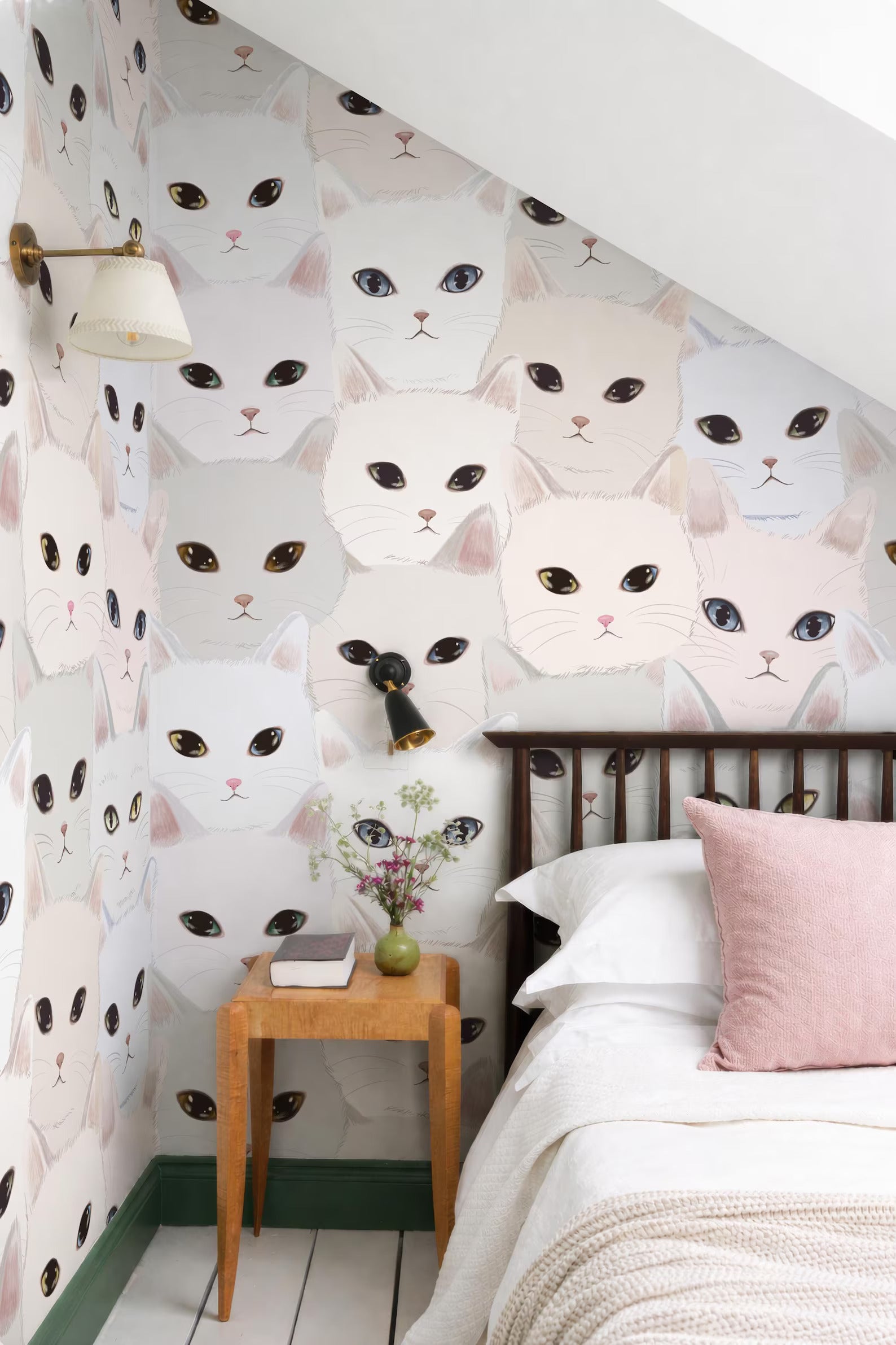 a bedroom with a white bed, a wooden nightstand, and a wallpapered wall with a repeating pattern of cat faces.