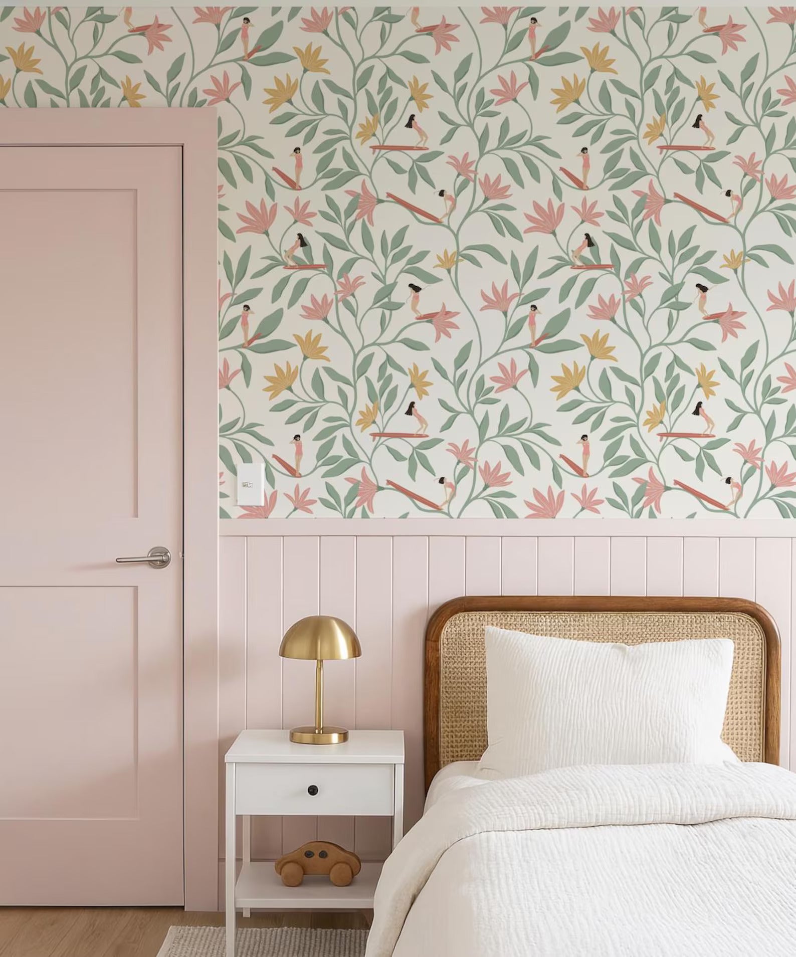 a bedroom with a pink door, a white bed with a wooden headboard, and a white nightstand with a lamp. The wall behind the bed has a floral wallpaper pattern in shades of pink, green, and yellow.