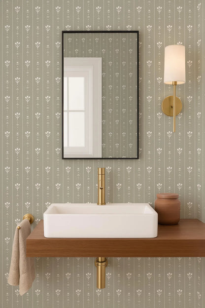 a bathroom with a white rectangular sink, a mirror above it, and a wooden shelf below the sink. The wall behind the sink has a patterned wallpaper with a repeating design of white flowers. There is also a light fixture mounted on the wall above the mirror.