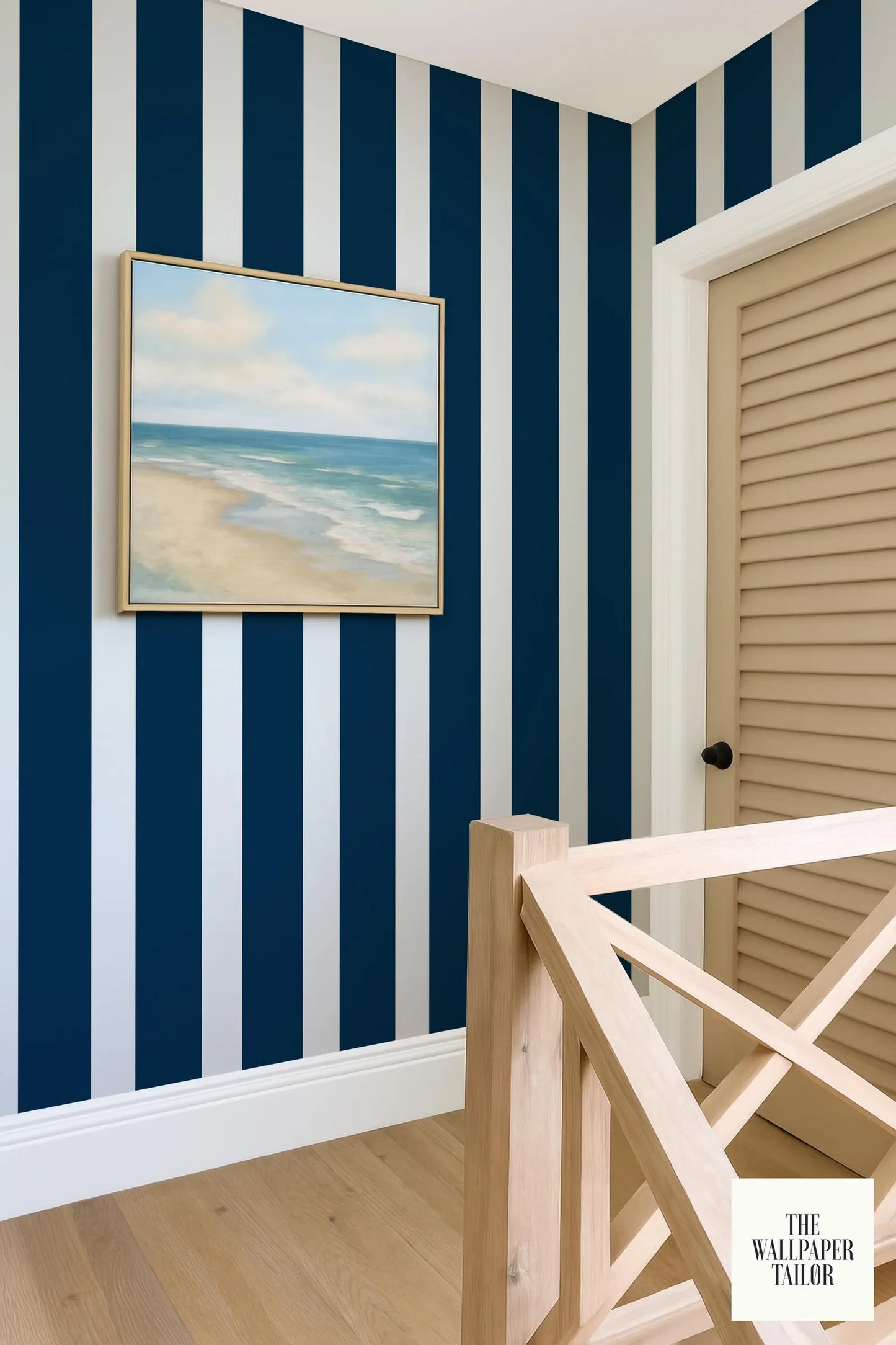 a room with blue and white striped walls, a wooden door, and a framed painting of a beach scene hanging on the wall.
