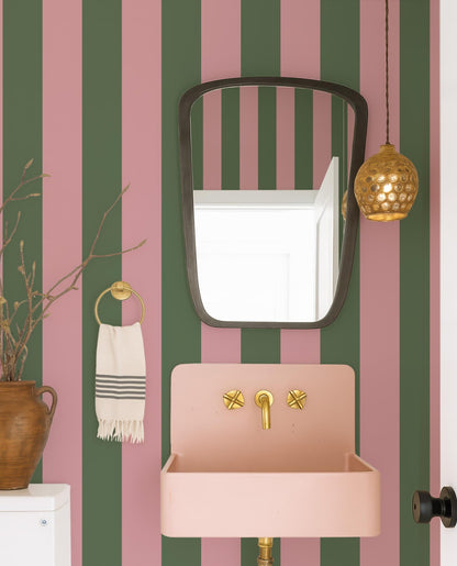 a bathroom with a pink sink, a mirror, and a hanging light fixture. The walls are striped in shades of green and pink, creating a vibrant and modern aesthetic.