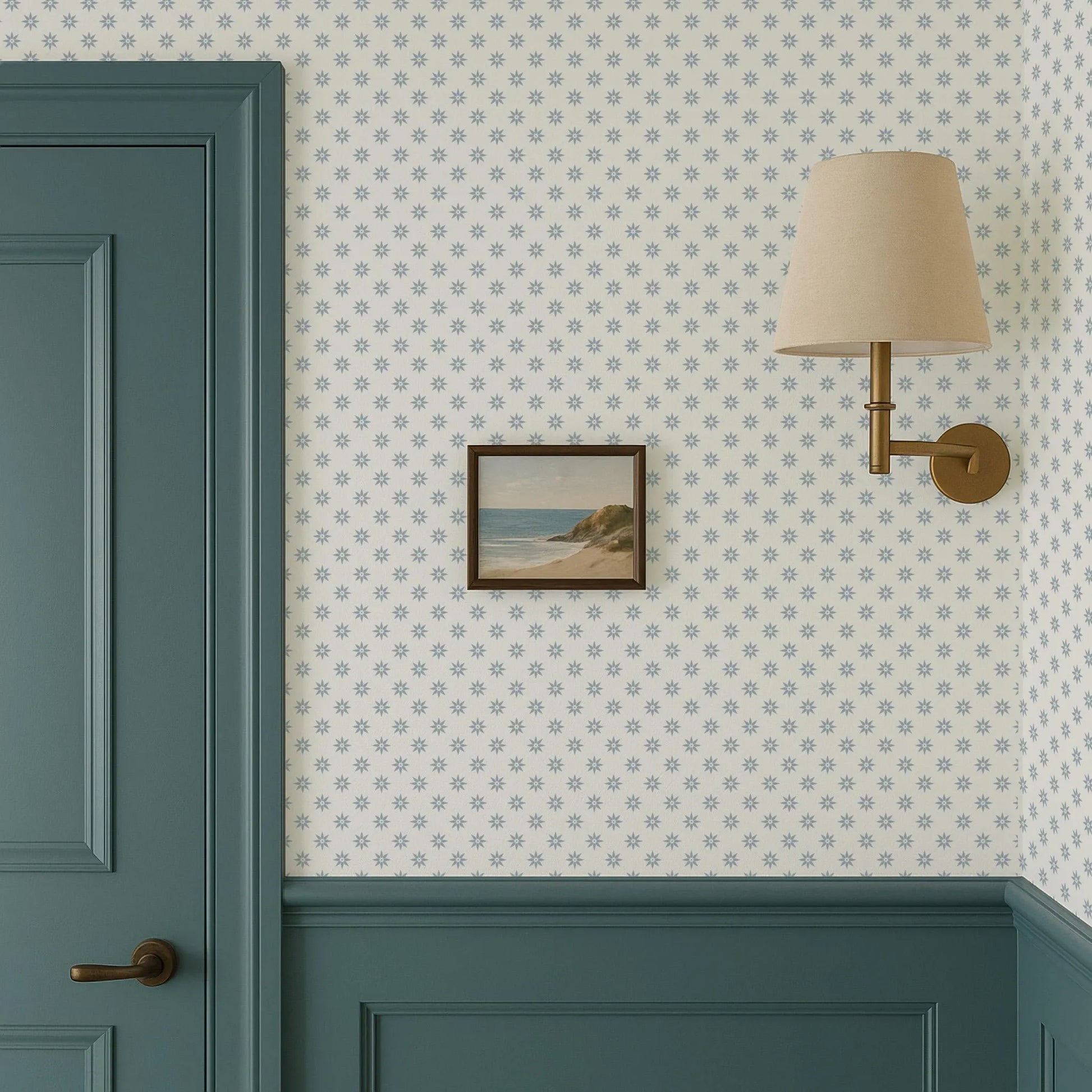 a wallpapered wall with a framed picture hanging on it, a green door, and a wall-mounted lamp.