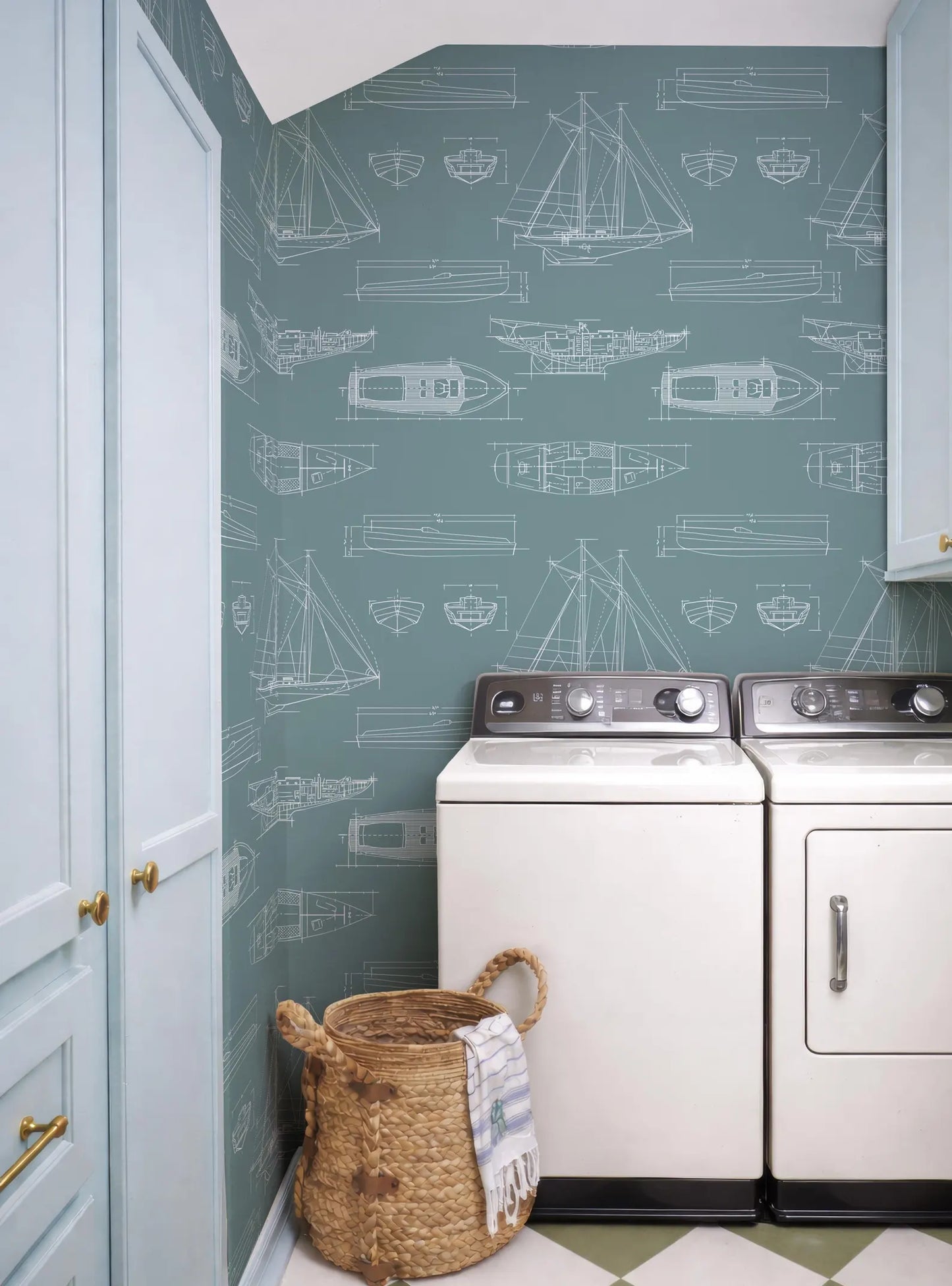 a laundry room with a blue and white color scheme, and a patterned wallpaper with illustrations of boats and ships. The room includes a washer and dryer, a basket, and a towel.