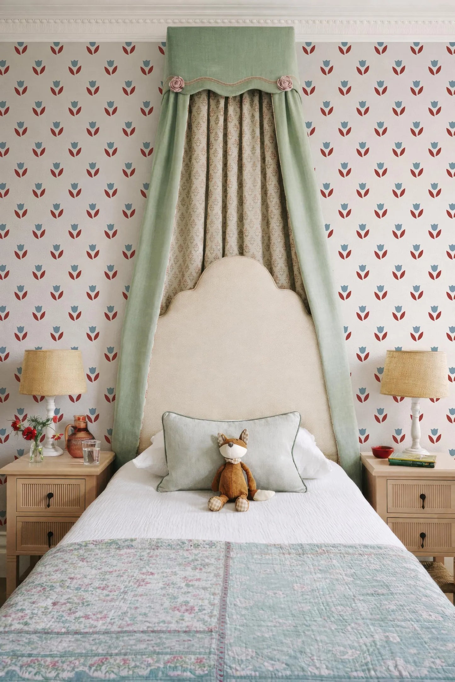 a cozy bedroom with a bed, nightstands, and a patterned wallpaper. A stuffed animal, specifically a cat, is sitting on the bed, adding a playful touch to the room.
