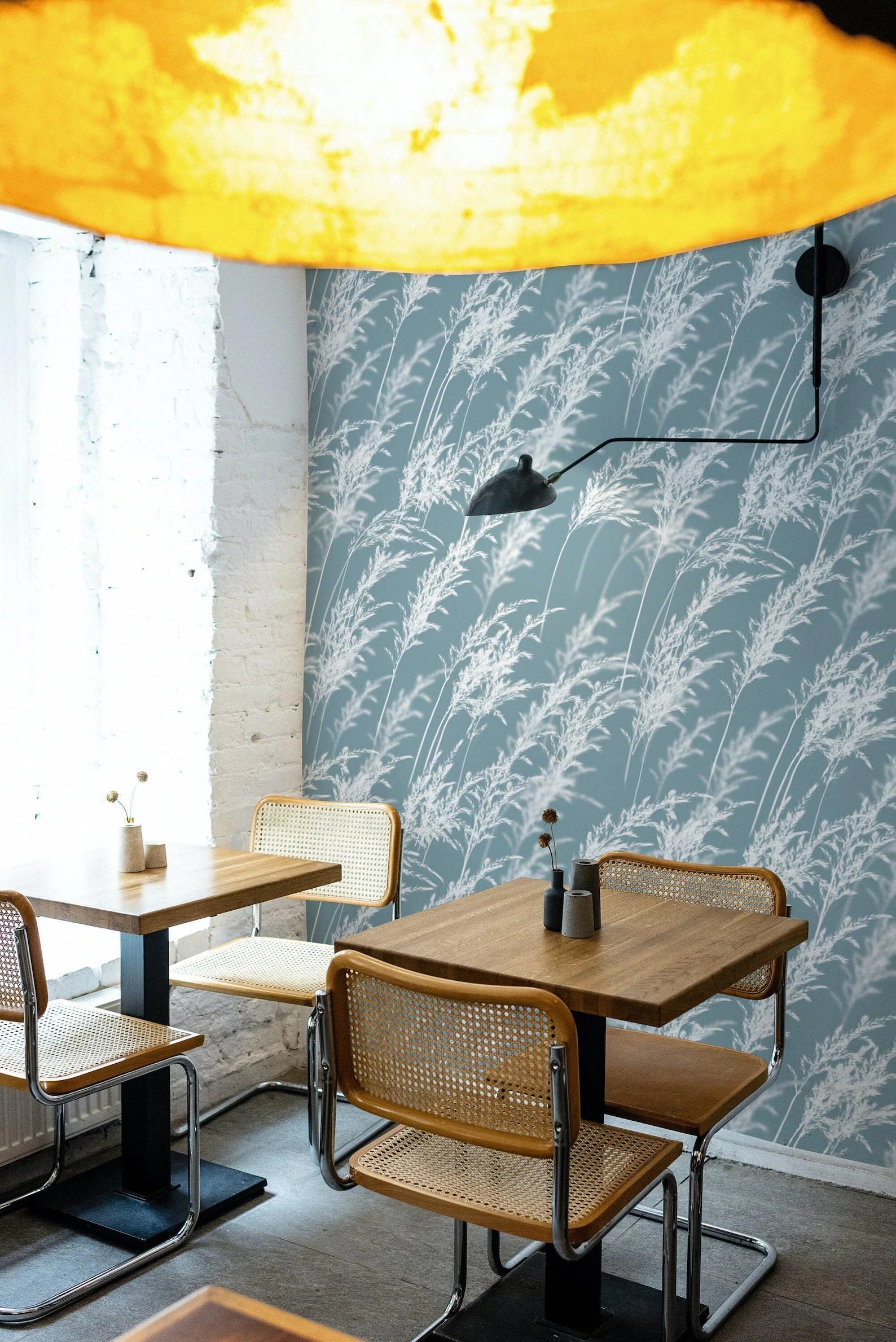 a modern dining area with a blue and white patterned wall, wooden tables and chairs, and a yellow light fixture hanging from the ceiling.