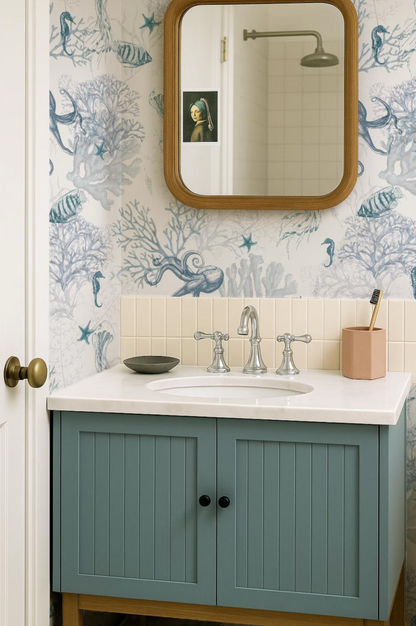 a bathroom with a blue and white patterned wallpaper, a white sink with a silver faucet, and a wooden-framed mirror above the sink.