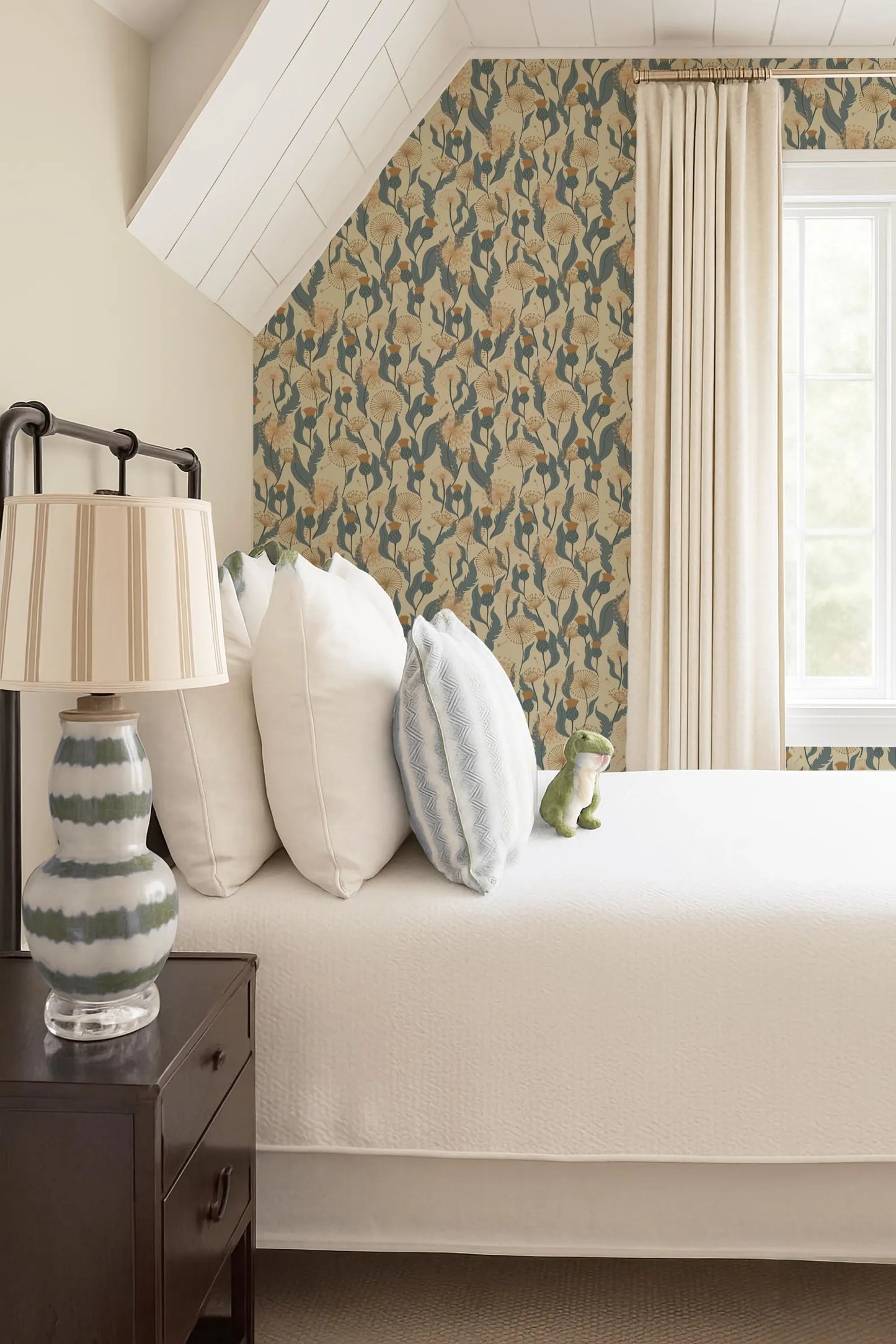 a cozy bedroom with a bed adorned with white pillows and a green and white striped pillowcase. A lamp with a striped shade is placed on a nightstand next to the bed. The room also features a window with curtains, and a patterned wallpaper on the wall.