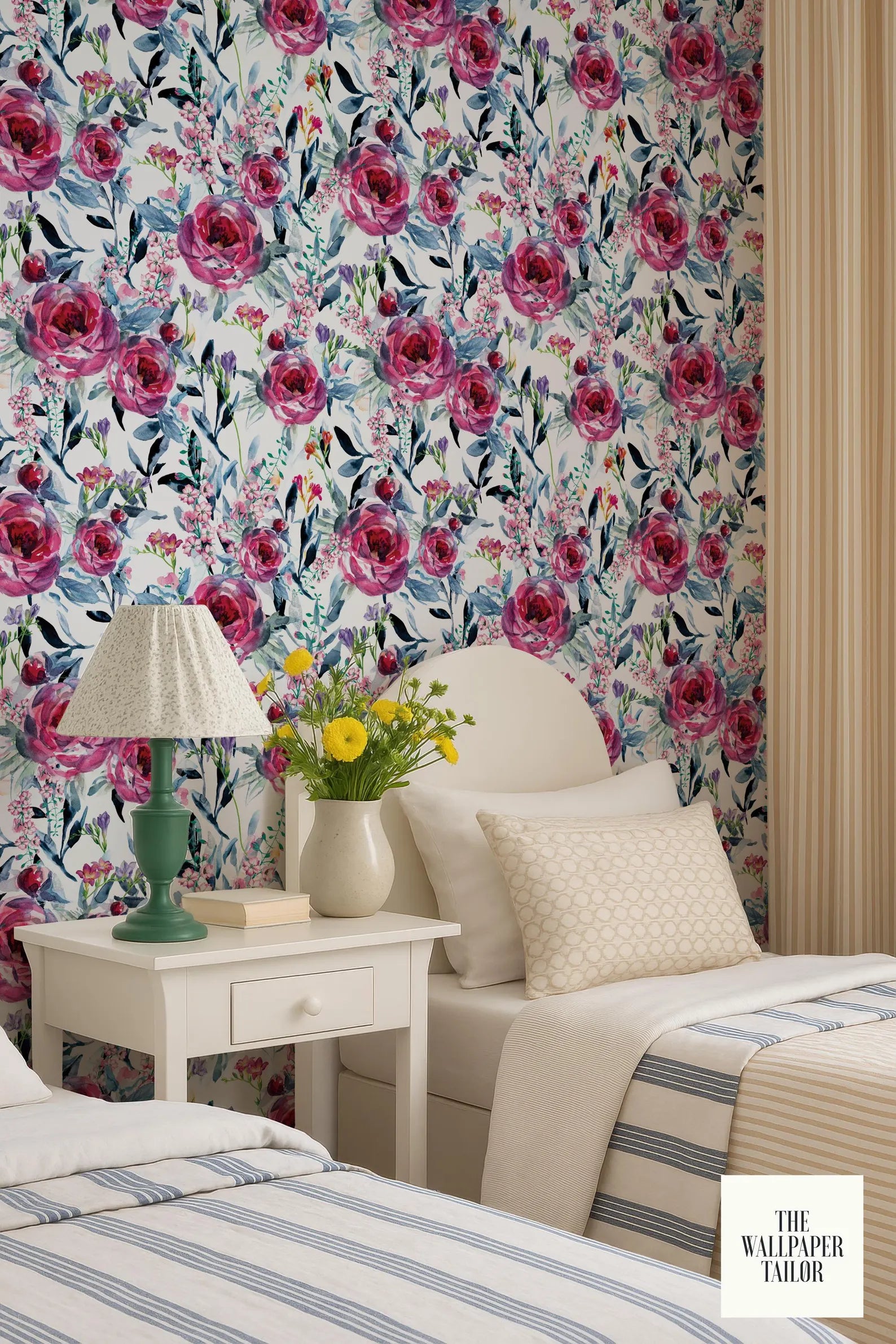 a bedroom with a floral wallpaper, a white bed with a striped blanket, a white nightstand with a lamp and a vase of yellow flowers, and a striped curtain.