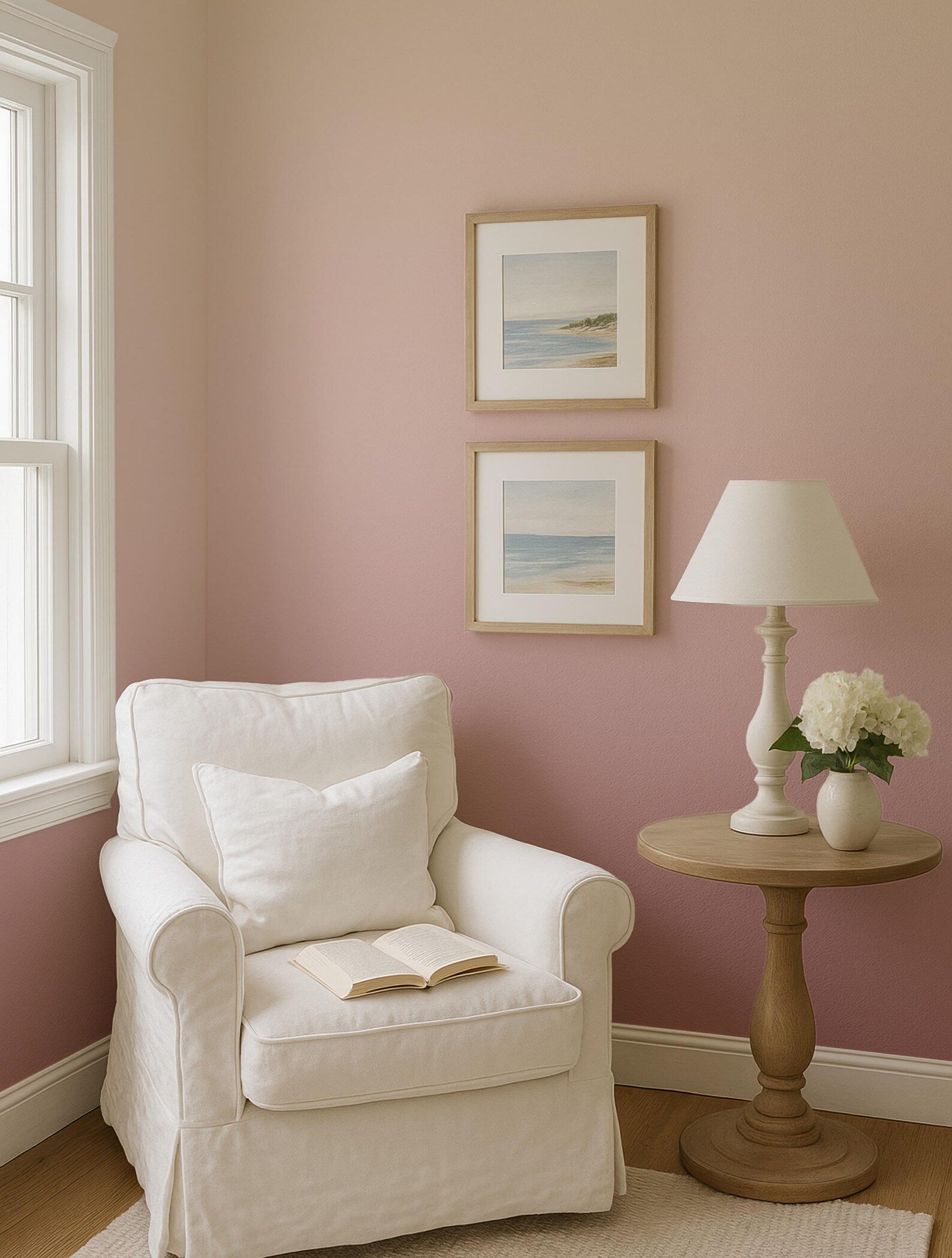A cozy corner of a room with a white armchair, a small side table with a lamp and a vase of flowers, and two framed pictures on the wall.