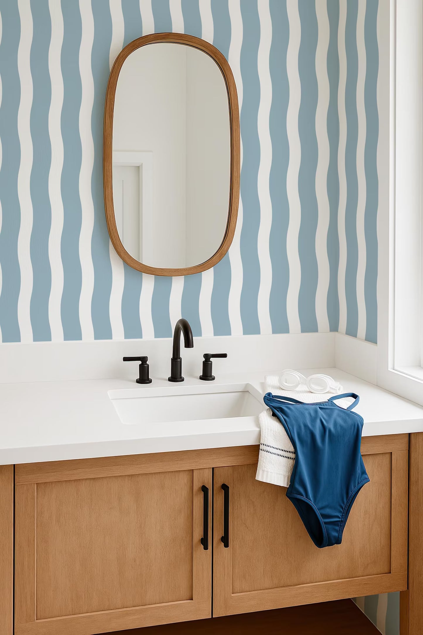a bathroom with a white sink, a mirror above it, and a blue swimsuit hanging on the side of the sink.