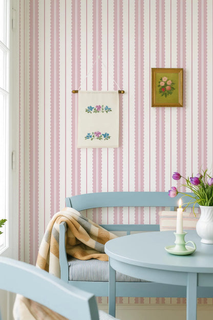 a cozy and charming dining area with a blue bench, a table with a candle, and a framed picture on the wall. The walls are adorned with pink and white striped wallpaper, and there are two paintings hanging above the table.