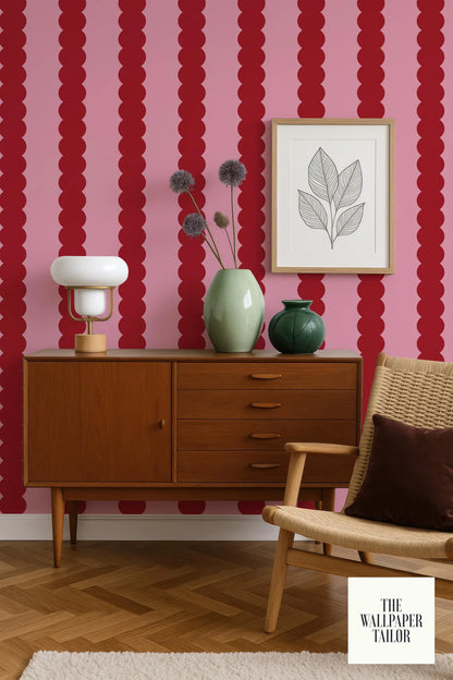 a modern living room with a wooden cabinet, a woven chair, and a framed artwork on the wall. The wall has a bold red and pink striped pattern, and the room has a warm, inviting atmosphere.