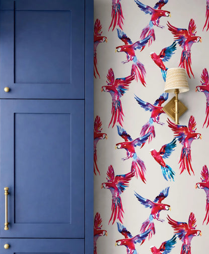 a vibrant wallpapered wall with a striking pattern of red and blue parrots in flight, complemented by a blue cabinet door and a gold-colored lamp fixture.