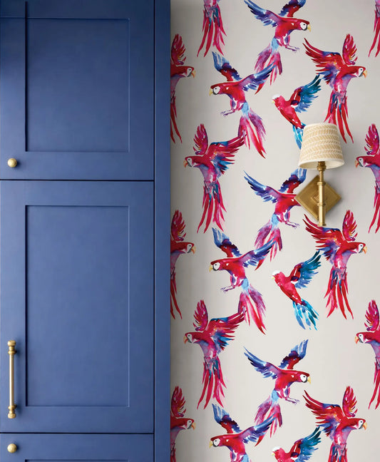 a vibrant wallpapered wall with a striking pattern of red and blue parrots in flight, complemented by a blue cabinet door and a gold-colored lamp fixture.