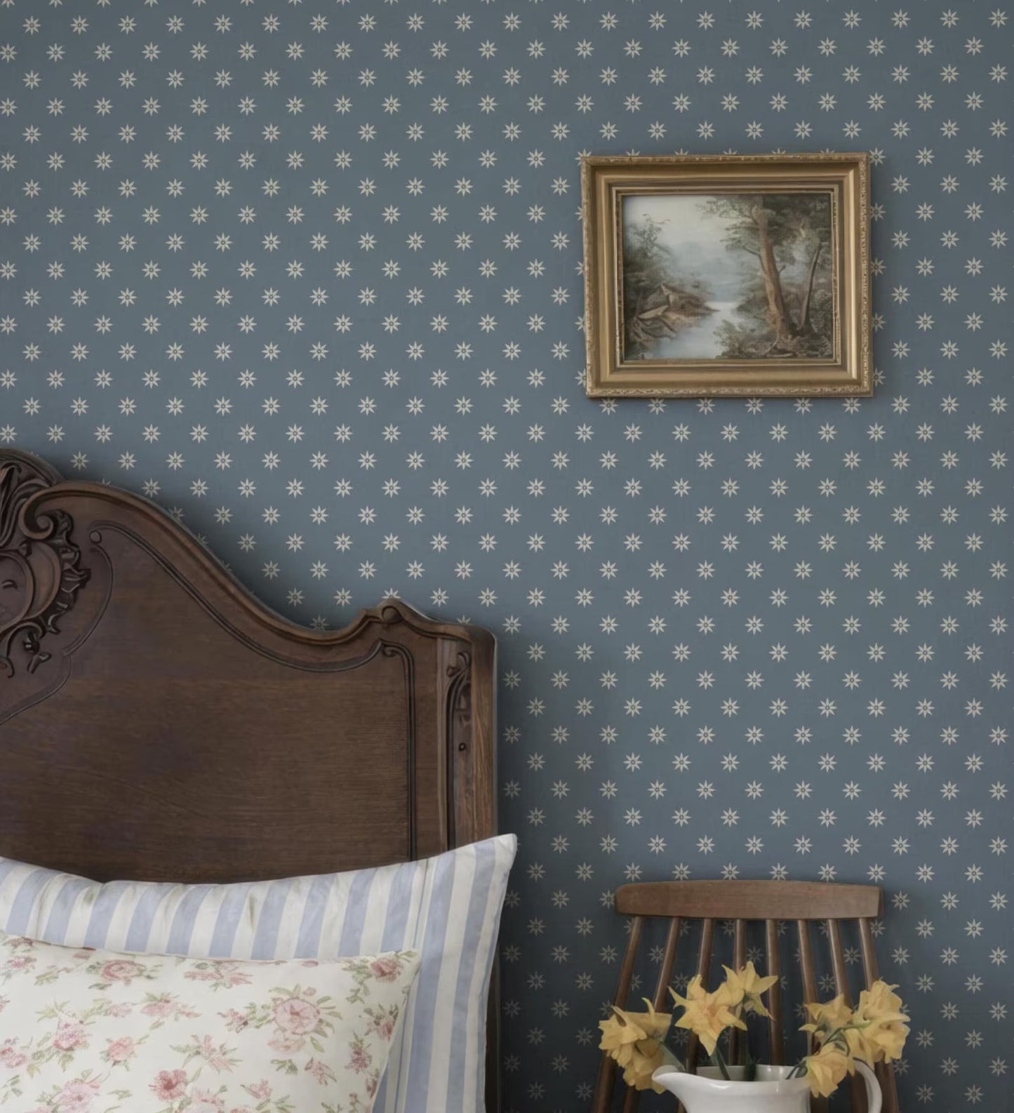 a bedroom with a wooden headboard, a framed landscape painting on the wall, and a wooden chair with yellow flowers on it.