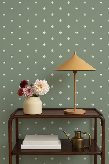 a wooden side table with a lamp, a vase with flowers, and a book on it. The table is set against a green wall with white polka dots.