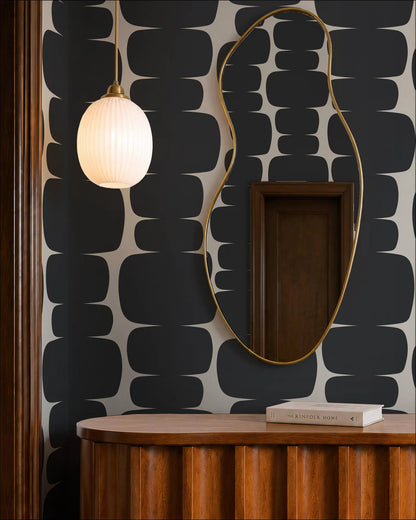 a modern interior design with a black and white geometric pattern on the wall, a wooden dresser, a round light fixture, and a large mirror with a gold frame.