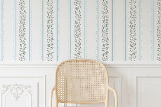 a cream-colored woven chair positioned against a wall with a decorative floral wallpaper.