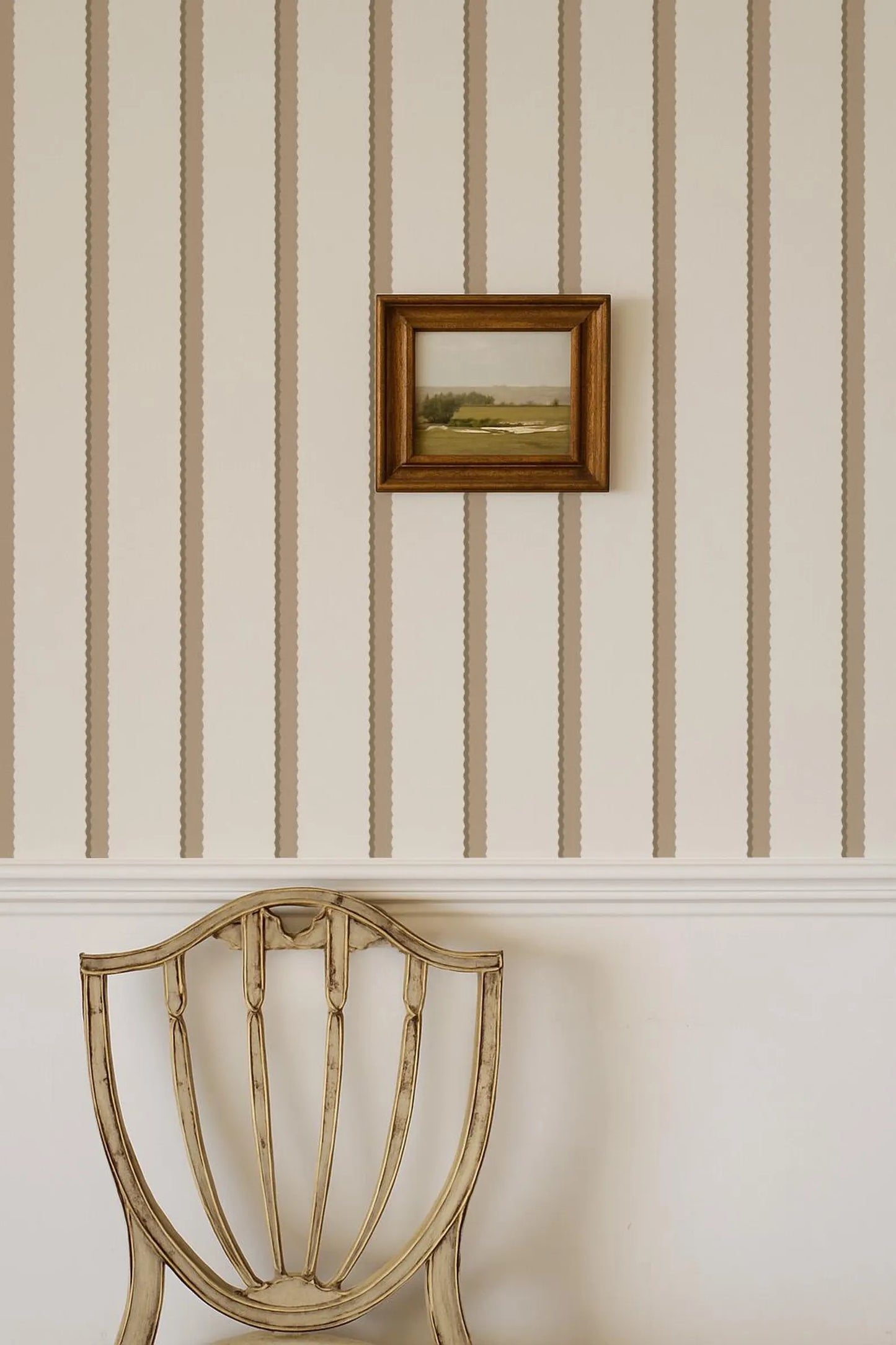 a wooden chair with a framed picture hanging on the wall above it.