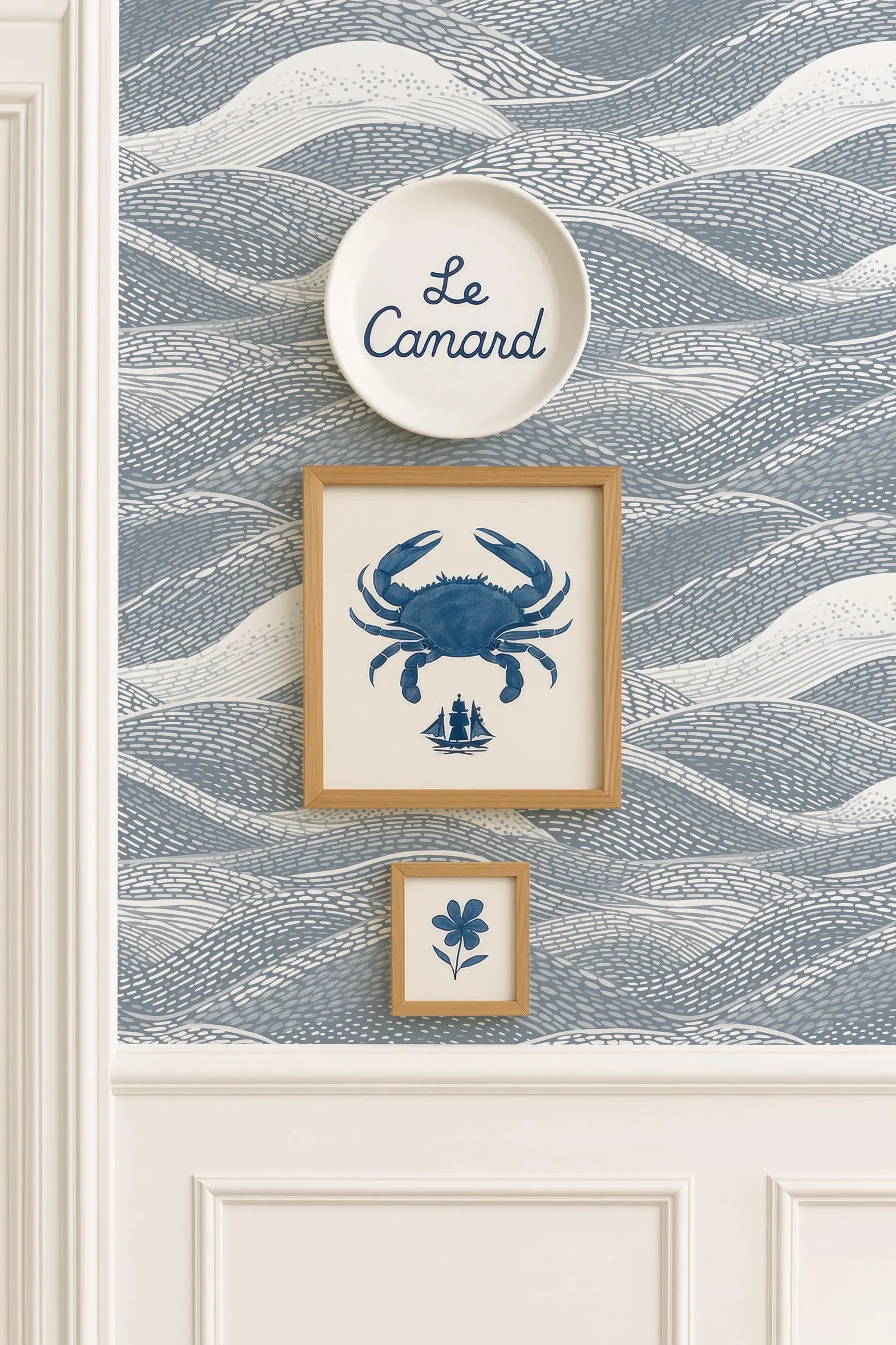 a wall with a blue and white wallpaper pattern, and there are three framed pictures hanging on it. The top picture is a large blue crab, the middle picture is a small blue flower, and the bottom picture is a small blue ship.