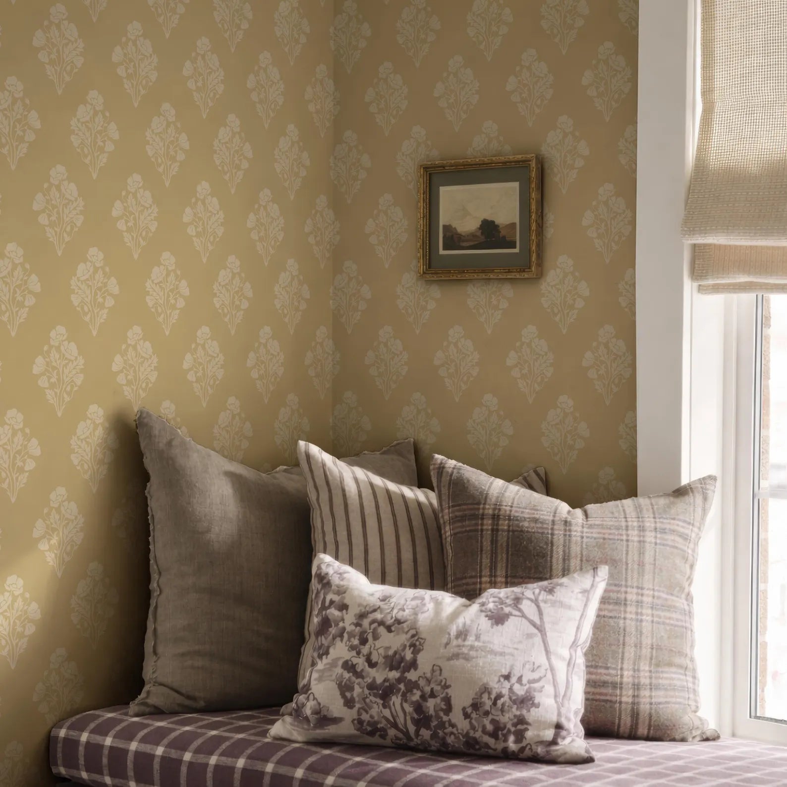 a cozy corner of a room with a window, featuring a bed with a floral patterned pillow and a framed picture on the wall.