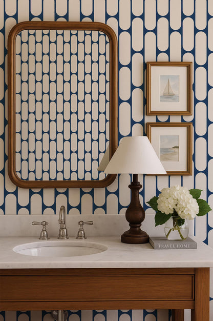 a bathroom with a white sink, a wooden vanity, a mirror, a lamp, and a framed picture of a sailboat. The wall behind the vanity has a blue and white geometric pattern.