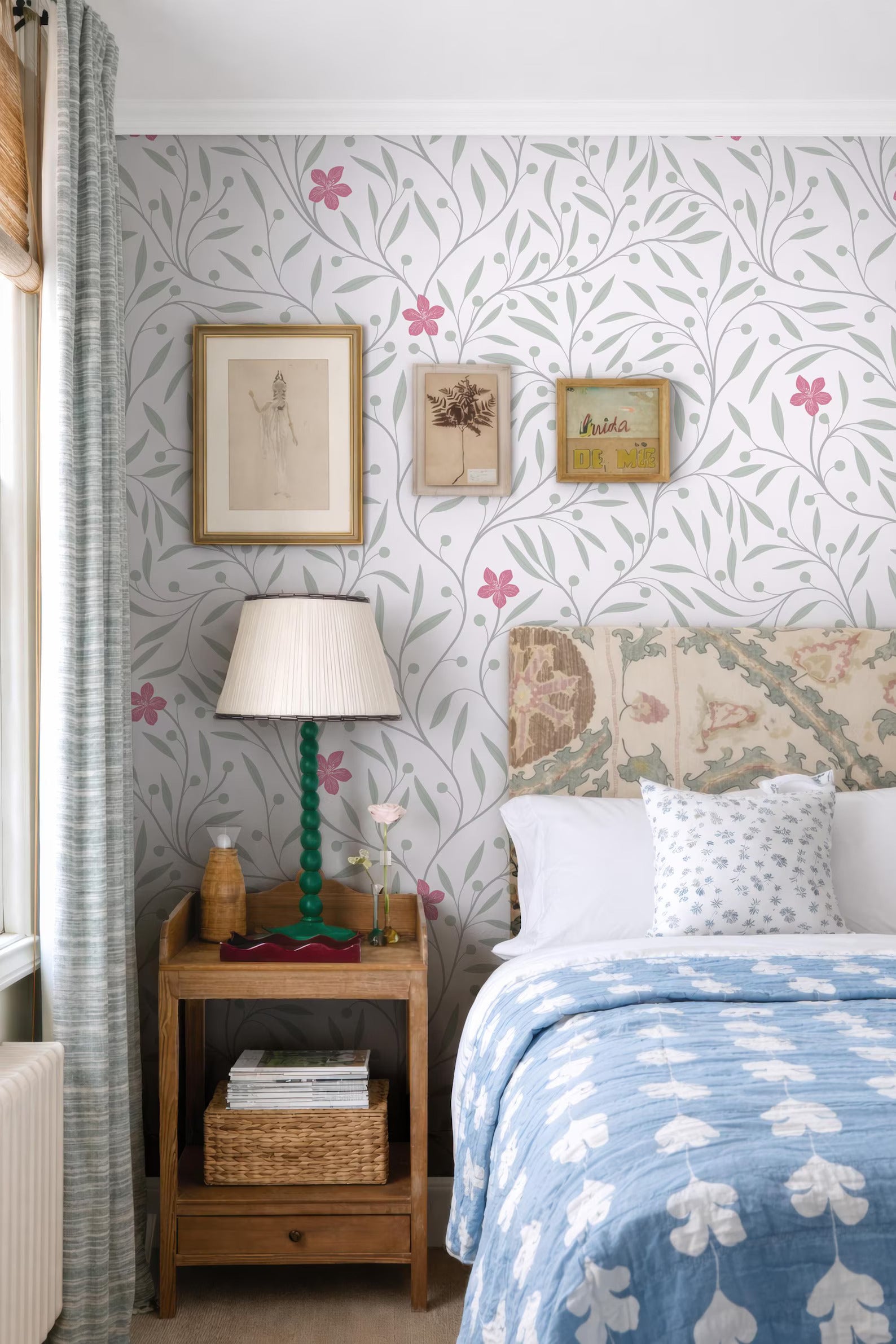a cozy bedroom with a floral wallpaper, a wooden nightstand, a lamp, and a bed with a blue and white patterned bedspread.