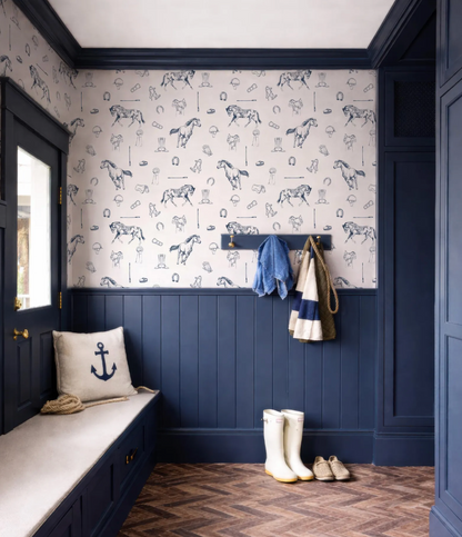 a room with a blue and white color scheme, including a patterned wallpaper with horses and other nautical elements. The room has a bench, a coat rack with a jacket and a scarf, and a pair of white boots.