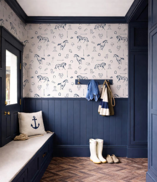 a room with a blue and white color scheme, including a patterned wallpaper with horses and other nautical elements. The room has a bench, a coat rack with a jacket and a scarf, and a pair of white boots.