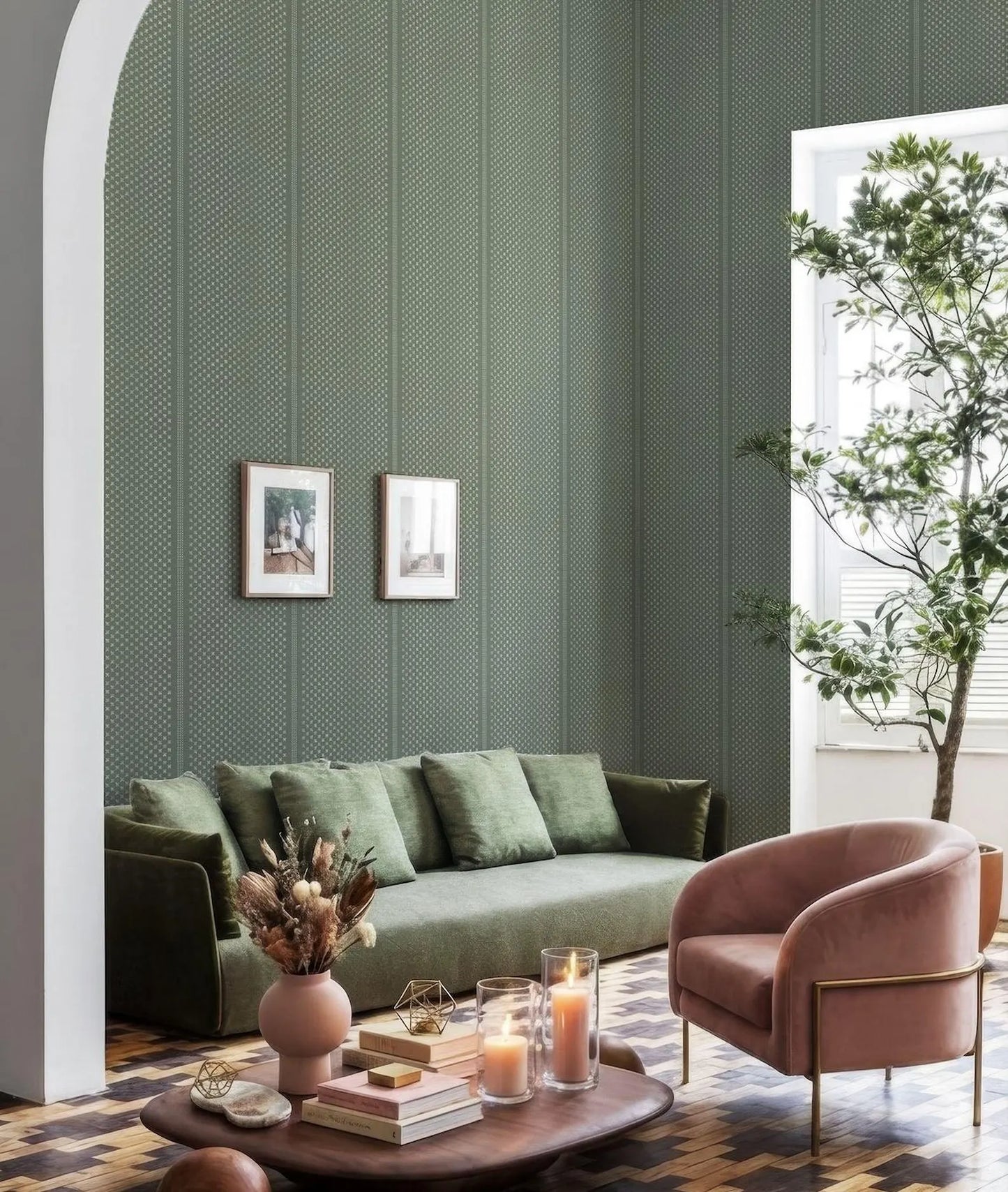 a cozy living room with a green sofa, a pink armchair, and a wooden coffee table. The room is decorated with a green patterned wallpaper, a white archway, and two framed pictures on the wall. There is also a potted plant and a vase of flowers on the coffee table, adding a touch of nature and color to the space.