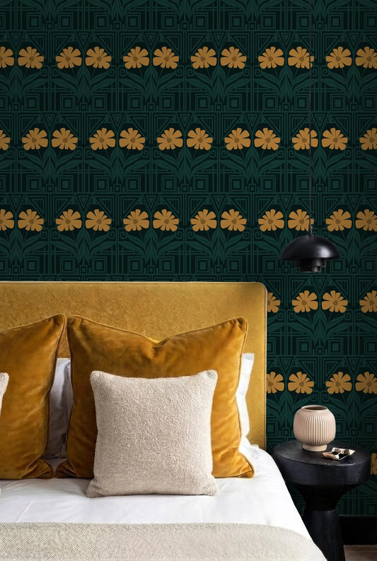 a bedroom with a bed, yellow and white pillows, and a black nightstand with a lamp. The wall behind the bed has a repeating pattern of yellow flowers in black and green.