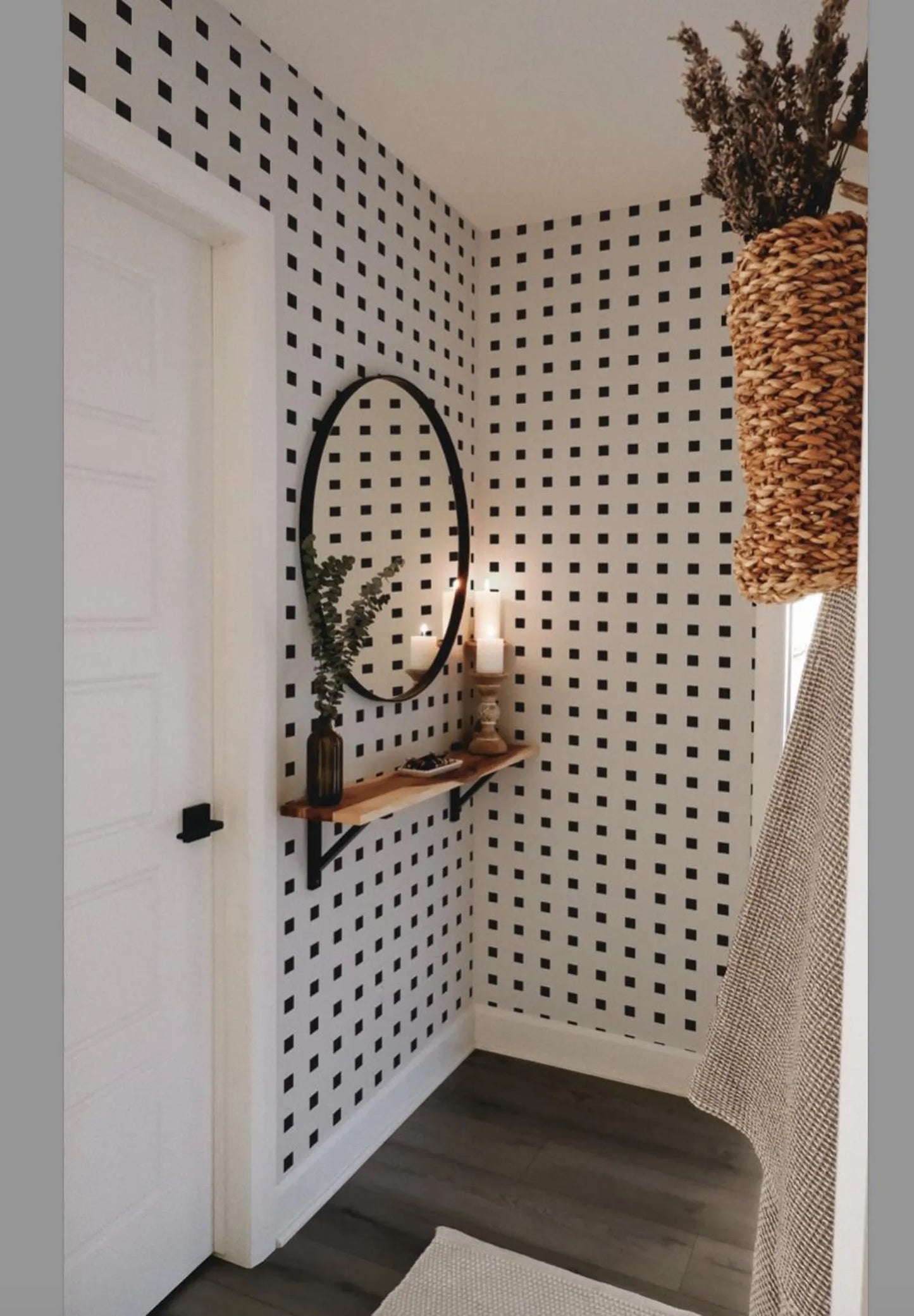 a bathroom with a black and white checkered pattern on the walls, a wooden shelf with a mirror and a plant, and a woven basket hanging on the wall.