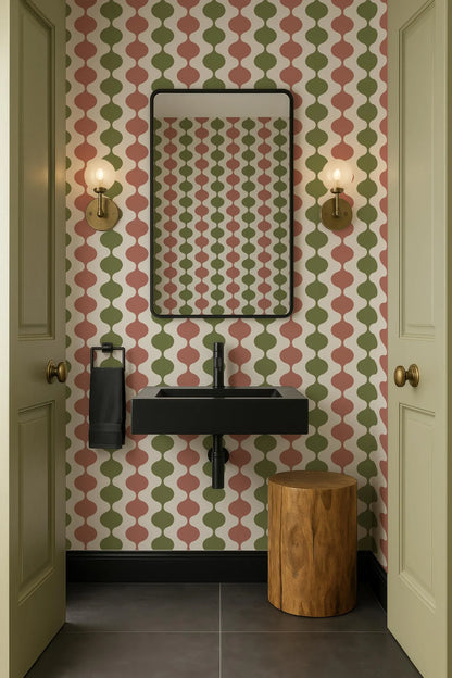 a bathroom with a black sink, a mirror, and two wall sconces. The walls are covered in a patterned wallpaper with a mix of green, red, and white colors. The floor is tiled, and there is a wooden stool in the corner of the room.