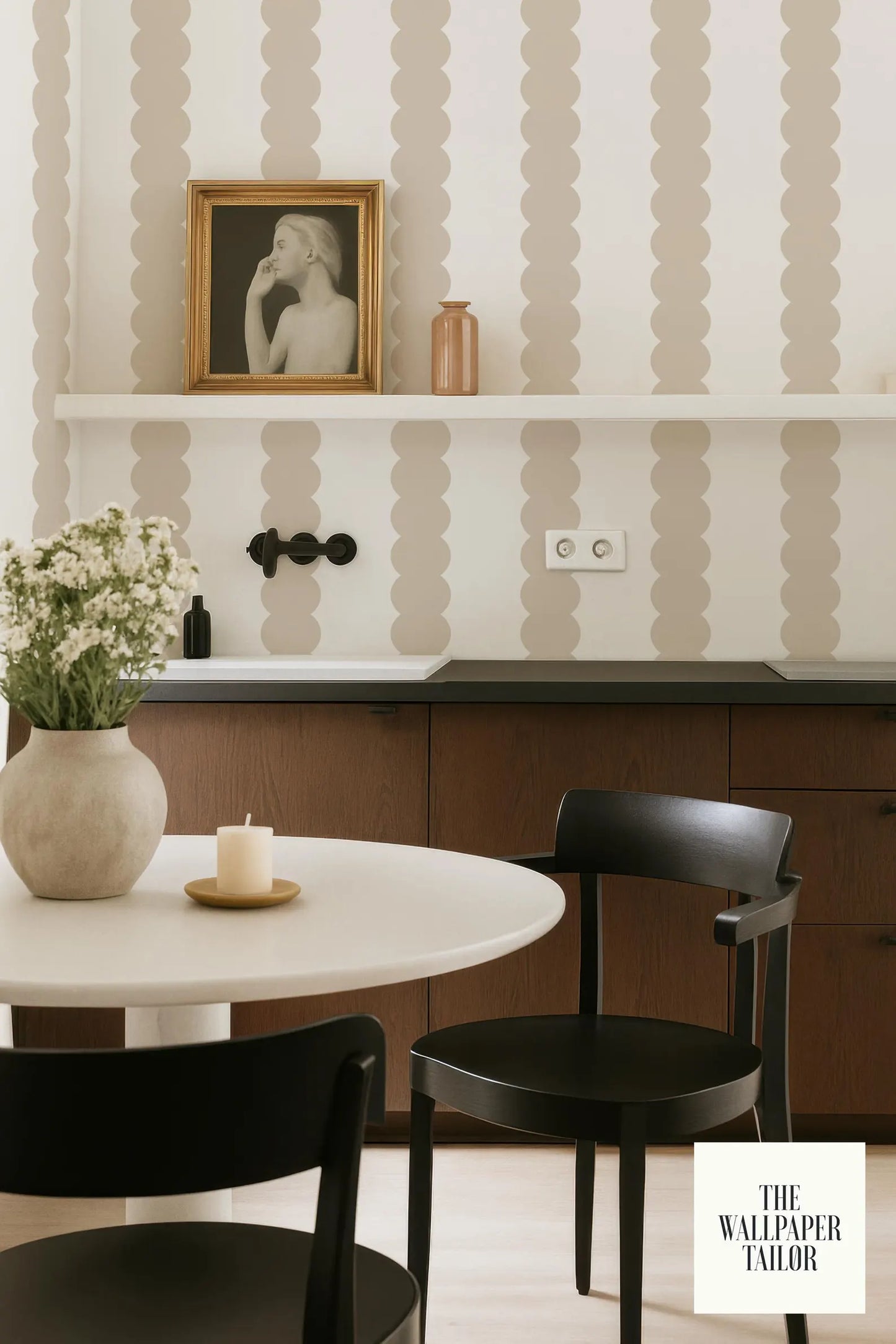 a modern kitchen with a white table, two black chairs, and a shelf with a framed picture and a vase of flowers.