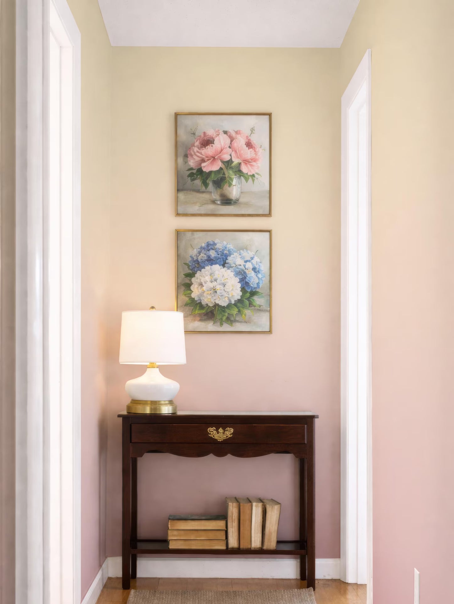 a cozy corner of a room with a wooden table, a lamp, and two framed paintings of flowers hanging on the wall above the table.