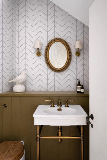 a bathroom with a white sink, a round mirror, and a white bird figurine on a shelf. The walls are covered in a chevron pattern, and there are two wall sconces above the sink.
