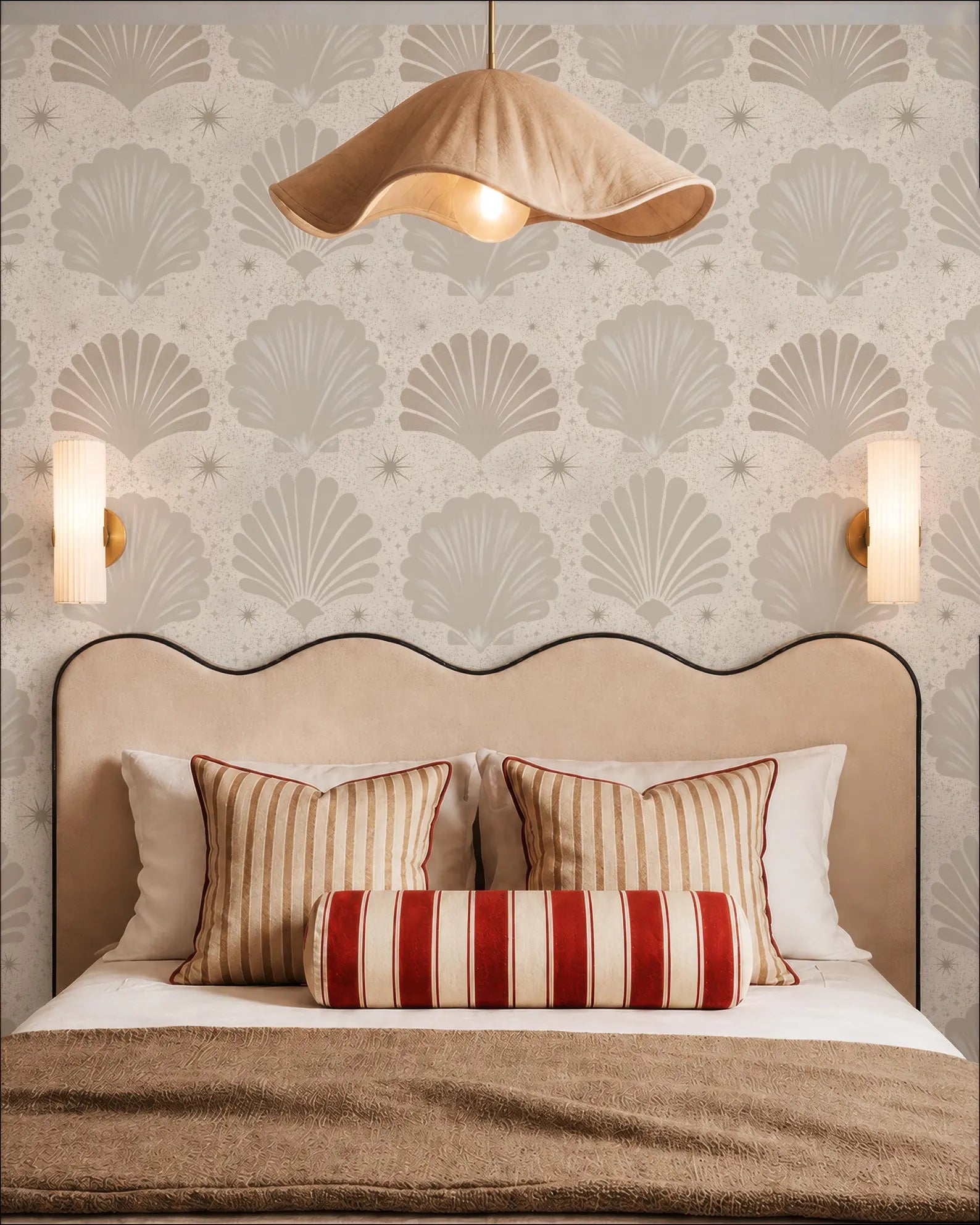 a well-decorated bedroom with a bed, two wall sconces, and a large, curved headboard. The walls are covered in a patterned wallpaper with a repeating shell motif, and the room has a warm, inviting atmosphere.