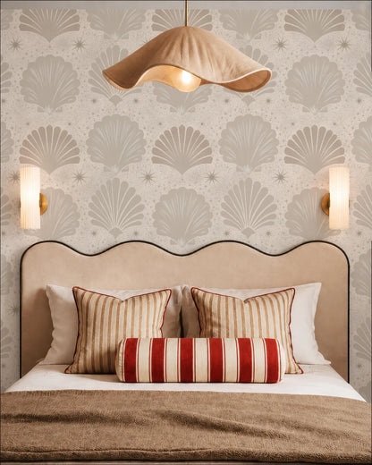 a well-decorated bedroom with a bed, two wall sconces, and a large, curved headboard. The walls are covered in a patterned wallpaper with a repeating shell motif, and the room has a warm, inviting atmosphere.