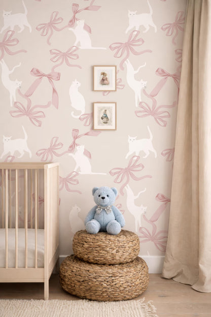 A baby's room with a wooden crib, a blue teddy bear, and a wall with a pink and white cat pattern wallpaper.