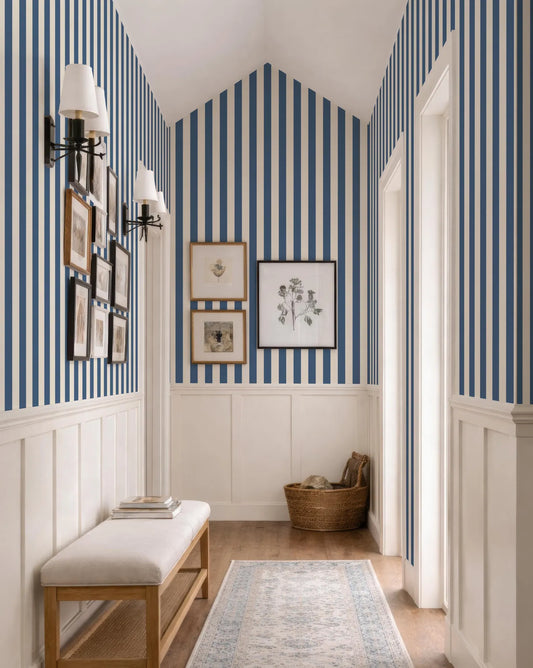 a hallway with blue and white striped walls, a wooden bench, and a woven basket on the floor. There are also framed pictures and artwork on the walls, creating a cozy and inviting atmosphere.