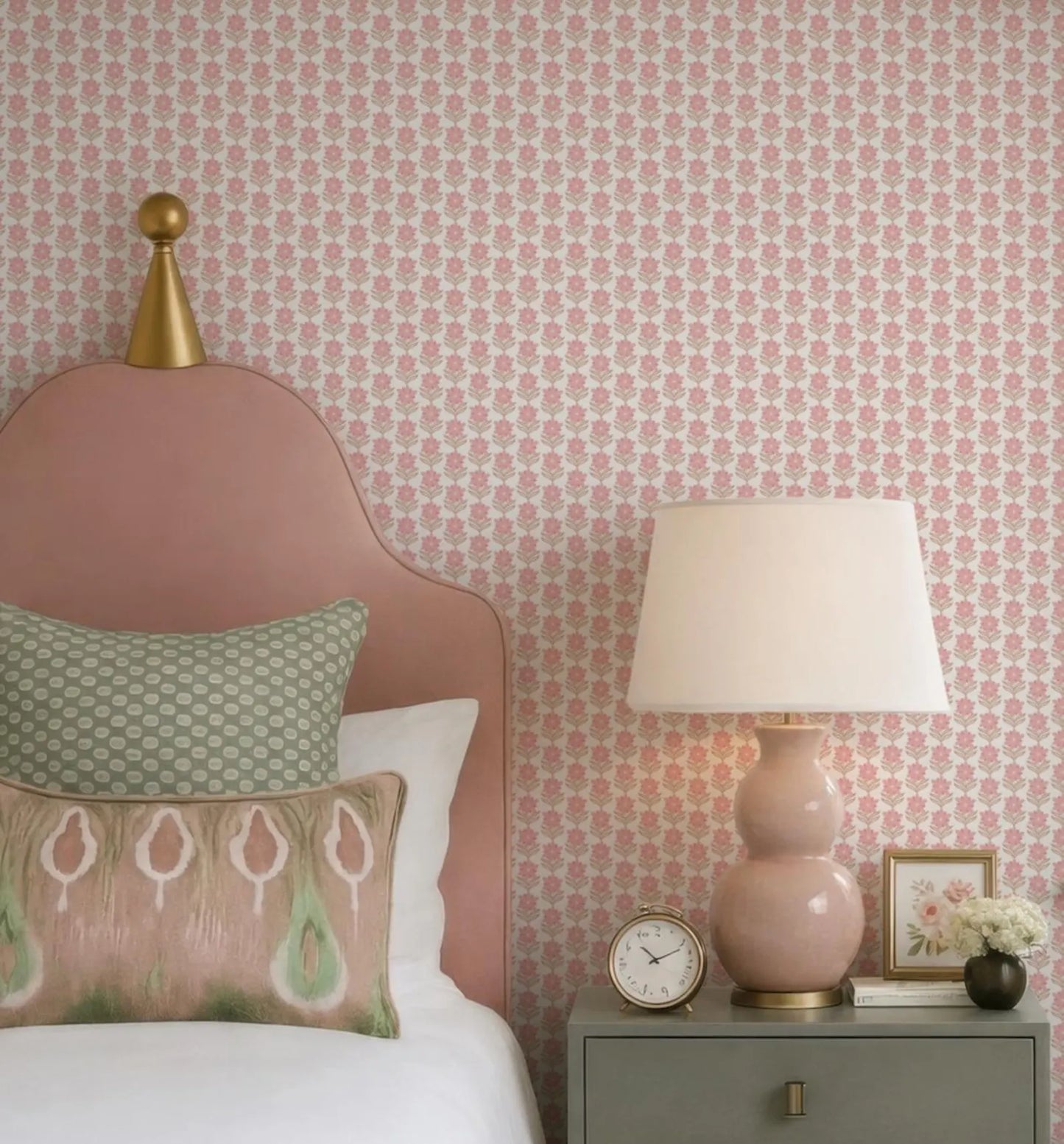 a bedroom with a pink headboard, a white bedspread, and a pink lamp on a nightstand. The wall behind the bed has a pink floral wallpaper.