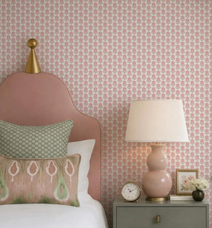a bedroom with a pink headboard, a white bedspread, and a pink lamp on a nightstand. The wall behind the bed has a pink floral wallpaper.
