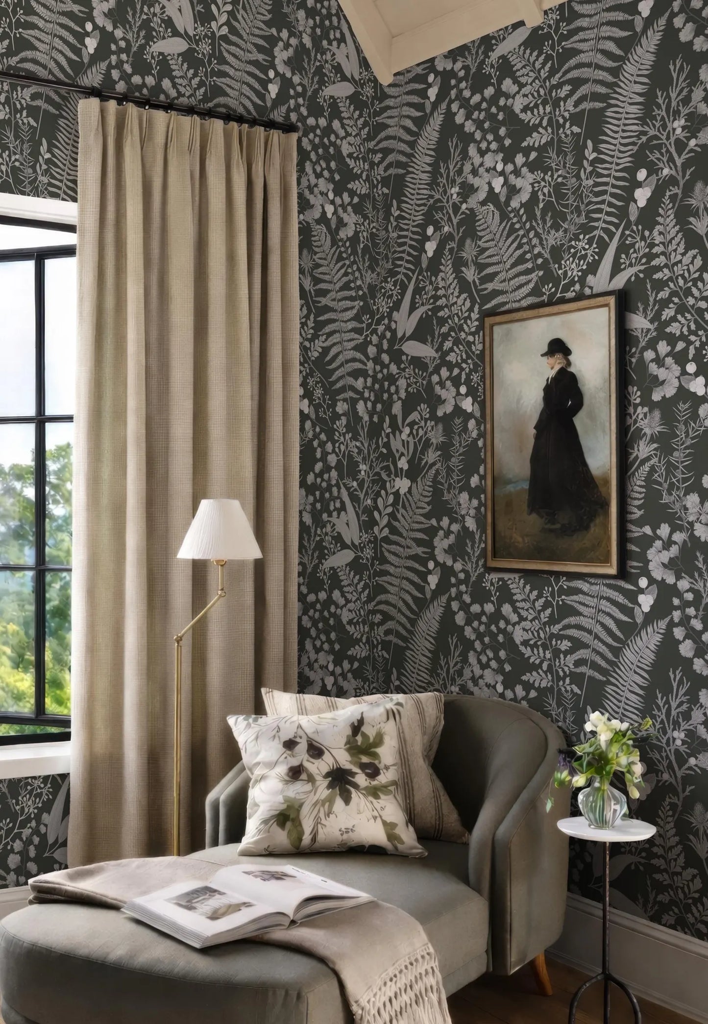 a cozy living room with a large window, a black and white floral wallpaper, a painting of a woman in a black dress, a gray armchair, a floor lamp, and a small side table with a vase of flowers.