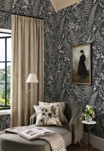 a cozy living room with a large window, a black and white floral wallpaper, a painting of a woman in a black dress, a gray armchair, a floor lamp, and a small side table with a vase of flowers.