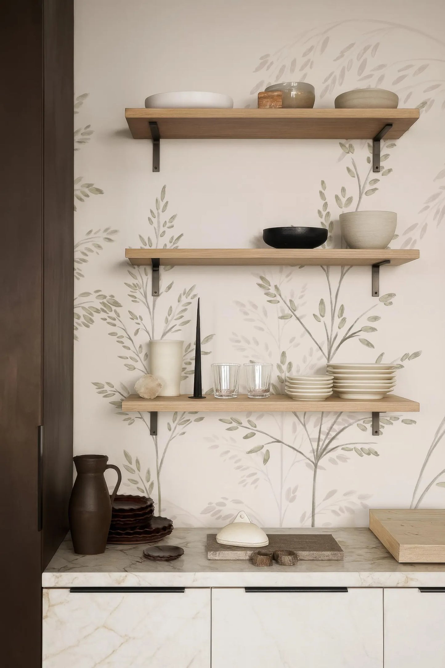 a kitchen counter with three wooden shelves displaying various kitchen items, including bowls, plates, and a vase.